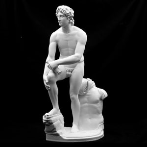 May include: White marble statue of a nude male figure standing on a rock base. The figure is holding a small object in his right hand and is looking to the left. The statue is on a black background.