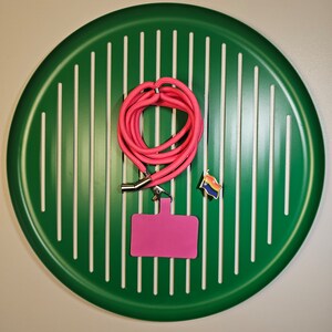 May include: A pink lanyard with a silver clip and a pink name tag on a green background with white stripes.