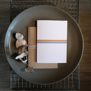 May include: A white card with a rainbow ribbon on a brown envelope, both sitting on a gray plate.