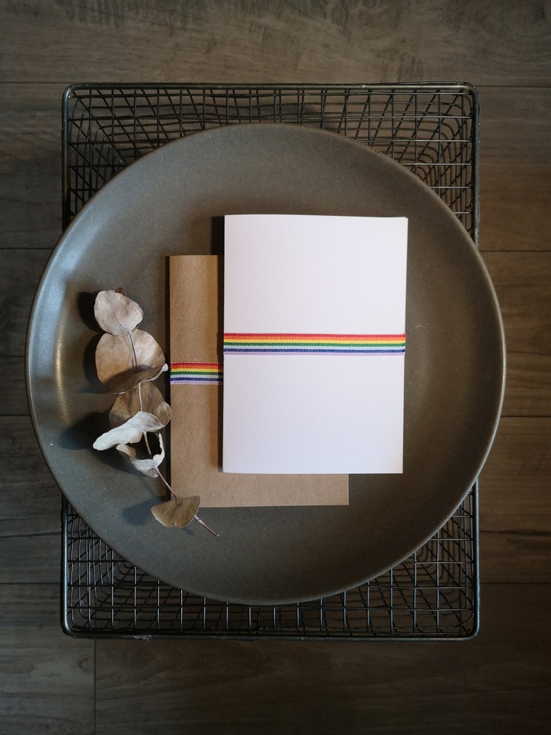 May include: A white card with a rainbow ribbon on a brown envelope, both sitting on a gray plate.