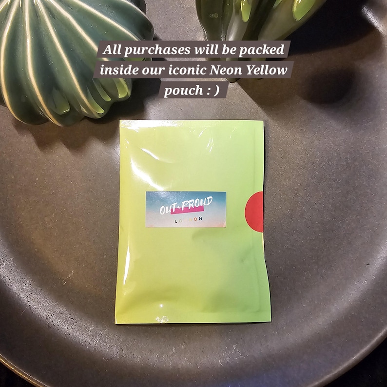 May include: A bright green pouch with the text "OUT-PROUD LONDON" printed on it. The pouch is sealed and has a red circle on the right side. The text "All purchases will be packed inside our iconic Neon Yellow pouch :)" is written above the pouch.