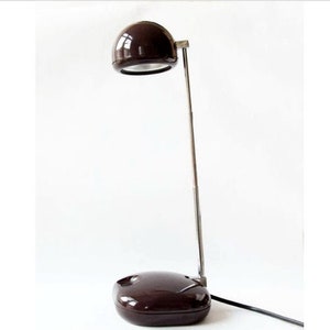 May include: A vintage brown desk lamp with a rounded shade and base. The lamp has a chrome-coloured adjustable arm and a black power cord. The design is minimalist and functional, suitable for a desk or bedside table.