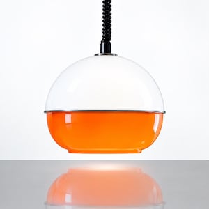 Könnte beinhalten: Eine kugelförmige Hängeleuchte mit zweifarbigem Design, bestehend aus einer glänzend weißen oberen Halbkugel und einer leuchtend orangefarbenen unteren Halbkugel, die durch ein schmales silbernes Band getrennt sind. Die Leuchte hängt an einem schwarzen Spiralkabel.