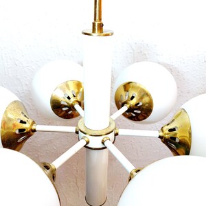K&ouml;nnte beinhalten: Ein wei&szlig;er und goldener Mid-Century-Modern-Kronleuchter mit sechs kugelf&ouml;rmigen Schirmen.