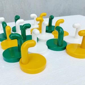 May include: A collection of colorful, decorative wall hooks. The hooks feature a circular base and a curved hook, in various colors including white, green, and yellow. The hooks are arranged on a white surface.