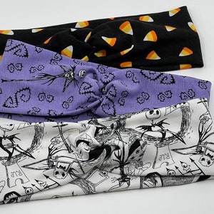 May include: Set of three Halloween themed fabric headbands. The first headband is black with orange candy corn designs. The second headband is purple with a white and black Jack Skellington design. The third headband is white with a black and white Jack Skellington design.