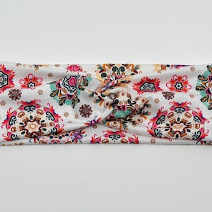 May include: A white headband with a colorful paisley pattern. The headband is twisted and has a knot in the center.