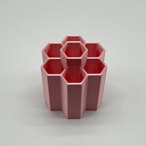 Pode incluir: Um organizador hexagonal rosa com seis compartimentos. O organizador &eacute; feito de pl&aacute;stico e tem um acabamento liso e fosco.