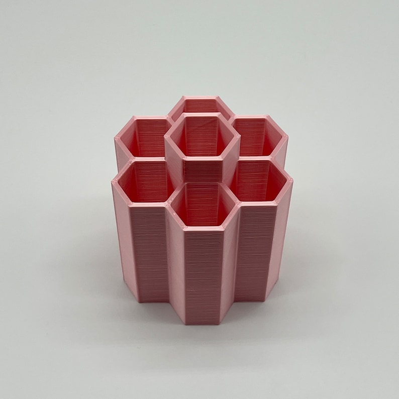 Pode incluir: Um organizador hexagonal rosa com seis compartimentos. O organizador &eacute; feito de pl&aacute;stico e tem um acabamento liso e fosco.