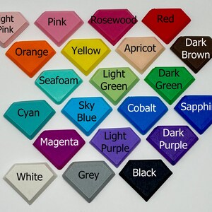 Pode incluir: Uma cole&ccedil;&atilde;o de 18 amostras de cor em forma de diamante, cada uma etiquetada com um nome de cor. As cores incluem rosa claro, rosa, pau-rosa, vermelho, laranja, amarelo, alperce, castanho escuro, espuma do mar, verde claro, verde escuro, ciano, azul celeste, cobalto, safira, magenta, roxo claro, roxo escuro, branco, cinzento e preto.