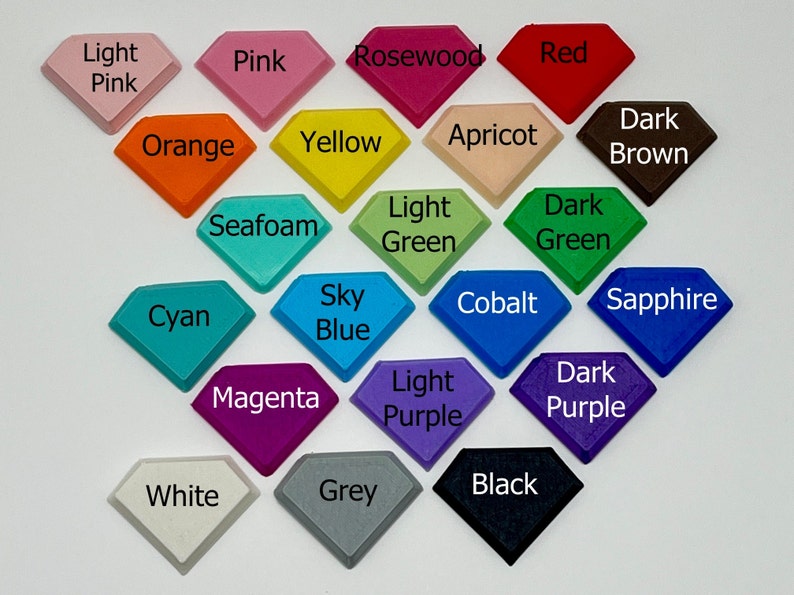 Pode incluir: Uma cole&ccedil;&atilde;o de 18 amostras de cor em forma de diamante, cada uma etiquetada com um nome de cor. As cores incluem rosa claro, rosa, pau-rosa, vermelho, laranja, amarelo, alperce, castanho escuro, espuma do mar, verde claro, verde escuro, ciano, azul celeste, cobalto, safira, magenta, roxo claro, roxo escuro, branco, cinzento e preto.