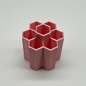 Pode incluir: Um organizador de mesa hexagonal rosa com seis compartimentos. O organizador &eacute; feito de pl&aacute;stico e tem um acabamento liso e fosco.