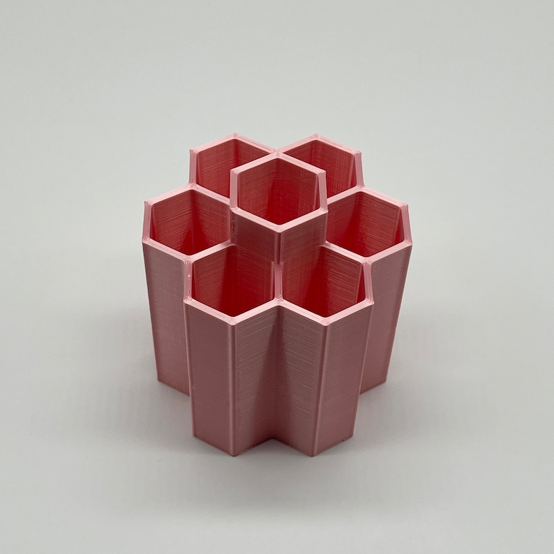 Pode incluir: Um organizador de mesa hexagonal rosa com seis compartimentos. O organizador &eacute; feito de pl&aacute;stico e tem um acabamento liso e fosco.