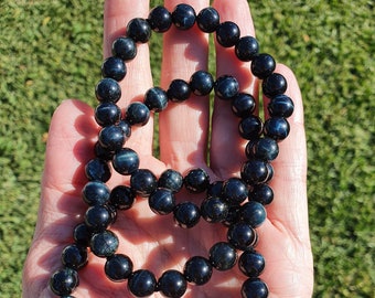 May include: Three black and blue gemstone bracelets with round beads. The bracelets are stacked on top of each other and are being held in a hand.