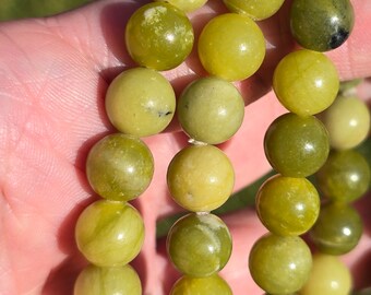 May include: A strand of green jade beads, each bead is round and smooth. The beads are strung together on a clear elastic cord.