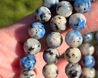 May include: A close-up of a beaded bracelet made with blue and white speckled stones. The bracelet is made with round beads and is stacked on top of itself.