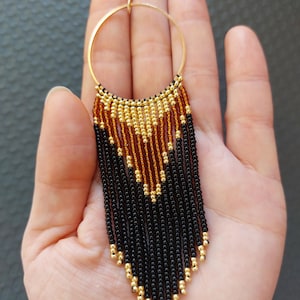May include: Gold hoop earrings with a black and gold beaded fringe. The fringe is made of small beads in a graduated pattern.