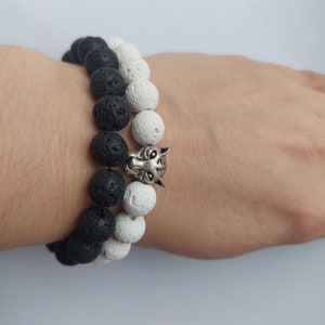 Könnte beinhalten: Schwarzes und weißes Armband aus Lavasteinen mit einem silbernen Wolfskopf-Anhänger.