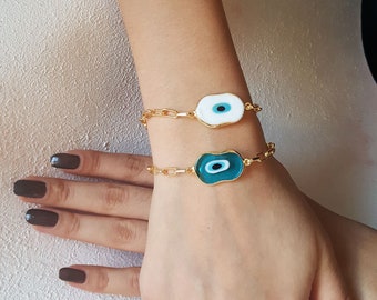 Può includere: Due braccialetti a catena dorata con ciondoli a forma di occhio turco blu e bianco. I ciondoli sono di forma ovale con un bordo dorato.