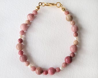 Puede incluir: Pulsera de cuentas con piedras preciosas rosas y beige. Cuenta con una cadena y un cierre dorados. Las cuentas, de varios tamaños y tonos, crean una joya delicada y atractiva.
