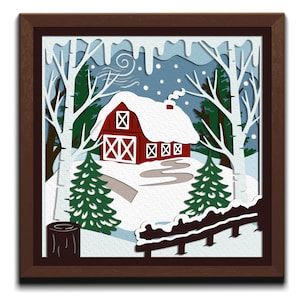May include: A framed paper cut art piece depicting a winter scene. A red barn with a snow-covered roof sits on a snowy hill, surrounded by white birch trees and evergreen trees. The artwork is set against a blue sky with falling snow.