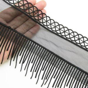 May include: A black trim featuring a sheer mesh base, a decorative lattice-style woven border along the top edge, and a series of long, thin, dangling fringe strands extending from the bottom edge of the mesh fabric.
