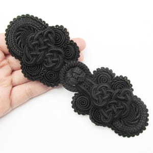 May include: Black fabric Chinese knot closure with intricate designs. This decorative button is perfect for adding a traditional touch to clothing or crafts.
