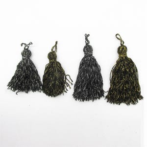 Puede incluir: Cuatro borlas decorativas dispuestas en fila, que incluyen dos borlas negras con hilos metálicos plateados y dos borlas negras con hilos metálicos dorados. Cada borla tiene un lazo superior anudado para colgar y flecos densos.