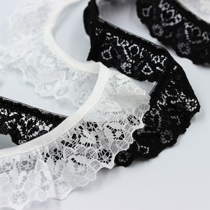 May include: Two pieces of lace trim, one white and one black, with a delicate floral pattern. The lace is ruffled and has a soft, flowing texture.