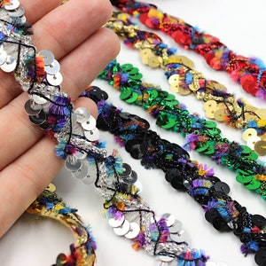 Può includere: Cinque diversi bordi di tessuto paillettes colorato con frange. I bordi sono argento, nero, verde, oro e rosso.