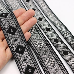 May include: Four black and silver trim ribbon with a geometric pattern. The ribbon is woven with a diamond pattern.