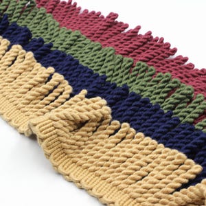 May include: Multicoloured twisted cord trim with a fringe. The trim is in four colours: beige, navy blue, forest green, and burgundy.