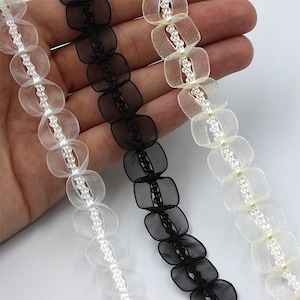 May include: Three strands of decorative trim with scalloped edges. The trim is made of sheer fabric with a beaded centre. The trim is available in white, black, and ivory.