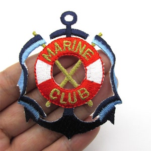 Könnte beinhalten: Ein gestickter Aufnäher mit einem roten und weißen Rettungsring, einem blauen Anker und dem Text "MARINE CLUB" in goldener Farbe.