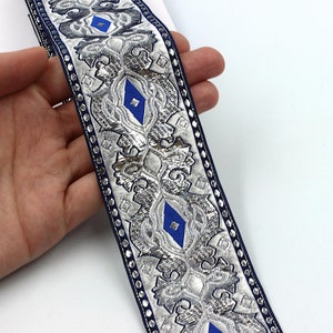 May include: Silver and blue trim with a repeating pattern of ornate silver designs and blue diamonds. The trim has a navy blue border with silver dots.