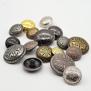 May include: Assortment of decorative metal buttons with ornate designs. The buttons are in various shades of silver, gold, and bronze.