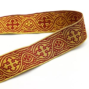 May include: A decorative ribbon with a repeating pattern of gold crosses and circular designs on a red background. The ribbon has a woven texture and a metallic sheen, suitable for craft projects and embellishments.
