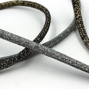 May include: Two cords of elastic trim with a sparkly finish. One cord is black with gold glitter, the other is silver with gray glitter.
