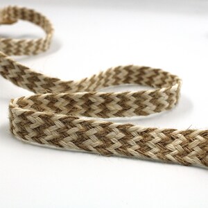 May include: Braided jute ribbon in natural beige and brown tones. The ribbon is woven in a chevron pattern, creating a textured and decorative element. Ideal for crafting, gift wrapping, or adding a rustic touch to various projects.