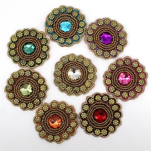 May include: Eight circular embroidered patches featuring a central faceted gemstone surrounded by concentric rings of metallic gold beads and small floral motifs. The gems appear in blue, purple, green, clear, pink, yellow, orange, and red colours.