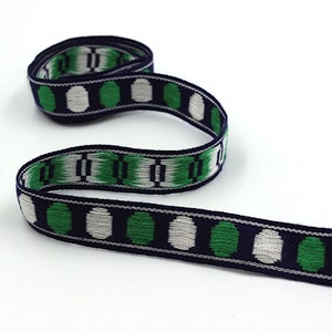 May include: A navy blue, white, and green woven ribbon with a repeating pattern of circles. The ribbon is approximately 1 inch wide.