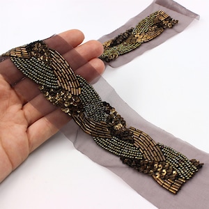 May include: A brown beaded and sequined trim with a wavy design. The trim is on a sheer brown fabric.