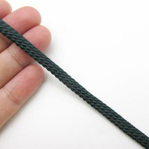 May include: A dark forest green cord featuring a tight, braided, and woven texture. The cord is cylindrical in shape and displays a consistent, uniform pattern throughout its length, showcasing a smooth, slightly reflective finish on the surface.