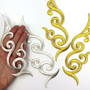 May include: Two sets of decorative iron-on patches. One set is silver and the other is gold. Both sets feature a swirling, floral design.