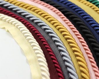 May include: Assortment of braided trim in various colors, including ivory, burgundy, gray, silver, gold, pink, and navy blue. The trim is made of a soft, woven material and has a rope-like texture.