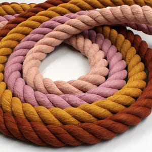 May include: A coiled rope in a spectrum of colours, including brown, gold, pink, and purple. The thick, twisted rope is arranged in a circular pattern, with each layer displaying a different hue. The rope's texture is visible, suggesting a natural fibre material.