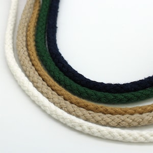 May include: A close-up shot of five braided ropes arranged in a curve. The ropes are in white, beige, brown, green, and navy. The thick ropes have a textured appearance, suitable for crafts and various projects.