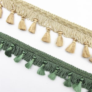 May include: Two decorative trims with tassels. One trim is beige with gold-coloured tassels, and the other is dark green with green tassels. Both trims have a wavy design along the top edge and fringe with tassels.