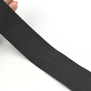 May include: Black woven ribbon with a raised embossed pattern. The pattern is a repeating design of stylised flowers.