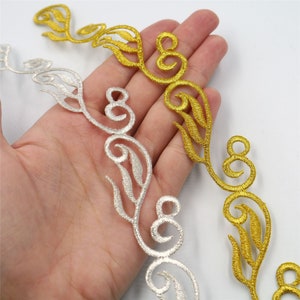 May include: Two lengths of decorative trim, one gold and one silver, with a floral design. The trim is made of embroidered thread and has a delicate, intricate pattern.